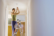 Photo: Woman doing DIY at home, standing on step ladder, attaching light bulb to ceiling fixture, smiling Woman doing DIY at home, standing on step ladder, attaching light bulb to ceiling fixture, smiling