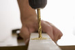 Photo: Man drilling hole in piece of timber on workbench, close-up, side view, focus on foreground Man drilling hole in piece of timber on workbench, close-up, side view, focus on foreground