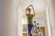 Photo: Woman doing DIY at home, standing on ladder, attaching light bulb to ceiling fixture, low angle view Woman doing DIY at home, standing on ladder, attaching light bulb to ceiling fixture, low angle view