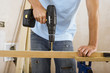 Photo: Man doing DIY at home, drilling hole in piece of timber on workbench, front view, mid-section Man doing DIY at home, drilling hole in piece of timber on workbench, front view, mid-section
