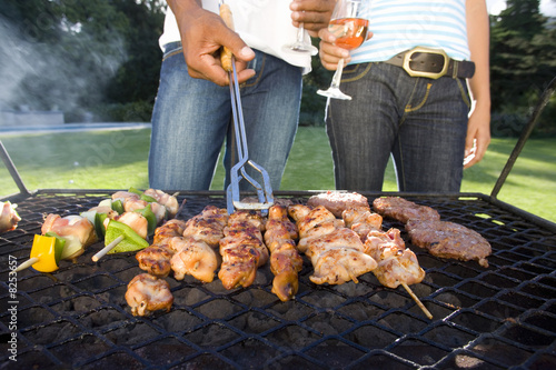 Photo: Couple having barbeque outdoors, standing by grill, mid section Couple having barbeque outdoors, standing by grill, mid section