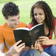 Two teens share bible in a park
