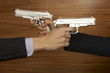Hands of two businessmen pointing guns at each other
