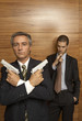 Photo: Portrait of a businessman holding handguns with another businessman smoking a cigar behind him Portrait of a businessman holding handguns with another businessman smoking a cigar behind him