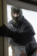 Masked thief braking in through window