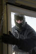 Masked thief braking in through window
