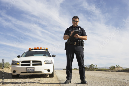 Photo: Police officer taking notes in front of police car Police officer taking notes in front of police car