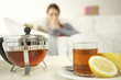 Photo: Close-up of herbal tea on a table with a mid adult woman sitting in the background Close-up of herbal tea on a table with a mid adult woman sitting in the background