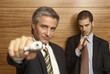Photo: Portrait of a businessman pointing a gun with another businessman smoking a cigar in the background Portrait of a businessman pointing a gun with another businessman smoking a cigar in the background