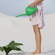 A woman watering a plant in the sand