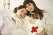 Photo: Portrait of two mid adult women leaning on each other's shoulders and holding a hot water bottle Portrait of two mid adult women leaning on each other's shoulders and holding a hot water bottle
