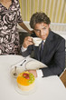 Photo: High angle view of a young man holding a cup of tea and sitting in front of a cake High angle view of a young man holding a cup of tea and sitting in front of a cake
