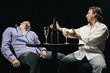 Young man lying unconscious on a table with another man sitting beside him