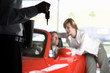 Photo: Couple looking at red convertible in car showroom, focus on salesman holding key in foreground Couple looking at red convertible in car showroom, focus on salesman holding key in foreground