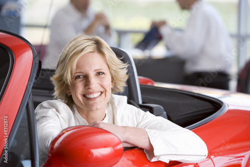Salesman with customer in car showroom, woman in red convertible in foreground, smiling, portrait Salesman with customer in car showroom, woman in red convertible in foreground, smiling, portrait