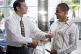 Photo: Salesman handing male customer key in car showroom, shaking hands, smiling, side view Salesman handing male customer key in car showroom, shaking hands, smiling, side view