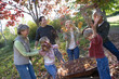 Photo: Multi-generational family collecting autumn leaves in wheelbarrow in garden, girl (7-9) throwing leaves Multi-generational family collecting autumn leaves in wheelbarrow in garden, girl (7-9) throwing leaves