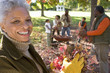 Photo: Multi-generational family collecting autumn leaves in garden, focus on grandmother standing in foreground, portrait Multi-generational family collecting autumn leaves in garden, focus on grandmother standing in foreground, portrait