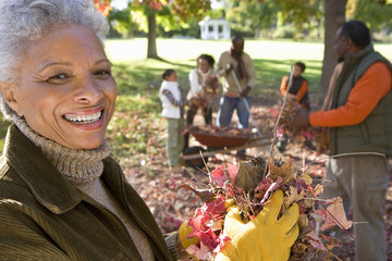 Photo: Multi-generational family collecting autumn leaves in garden, focus on grandmother standing in foreground, portrait Multi-generational family collecting autumn leaves in garden, focus on grandmother standing in foreground, portrait