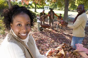 Photo: Multi-generational family collecting autumn leaves in garden, focus on mother standing in foreground, portrait Multi-generational family collecting autumn leaves in garden, focus on mother standing in foreground, portrait