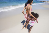 Photo: Mother and daughter (6-8) walking along sandy beach near water's edge, arms around each other, rear view Mother and daughter (6-8) walking along sandy beach near water's edge, arms around each other, rear view