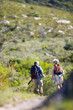 Photo: Mature couple hiking on mountain trail, carrying hiking poles and rucksacks, rear view Mature couple hiking on mountain trail, carrying hiking poles and rucksacks, rear view