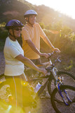Photo: Mature couple standing with bicyles on mountain trail in bright sunlight, looking at scenery (lens flare) Mature couple standing with bicyles on mountain trail in bright sunlight, looking at scenery (lens flare)