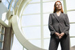 Photo: Confident businesswoman, with ginger hair, wearing grey suit, standing beside window, portrait, low angle view Confident businesswoman, with ginger hair, wearing grey suit, standing beside window, portrait, low angle view