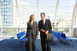 Photo: Businessman and woman walking with luggage in tow in airport departure lounge, smiling, front view Businessman and woman walking with luggage in tow in airport departure lounge, smiling, front view
