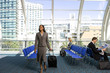Photo: Businesswoman walking in airport departure lounge with luggage in tow, businessman reading newspaper Businesswoman walking in airport departure lounge with luggage in tow, businessman reading newspaper