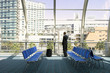 Photo: Solitary businessman waiting in airport departure lounge, looking through large window at urban scene, rear view Solitary businessman waiting in airport departure lounge, looking through large window at urban scene, rear view