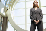 Photo: Confident businesswoman, with ginger hair, wearing grey suit, standing beside window, portrait, low angle view Confident businesswoman, with ginger hair, wearing grey suit, standing beside window, portrait, low angle view