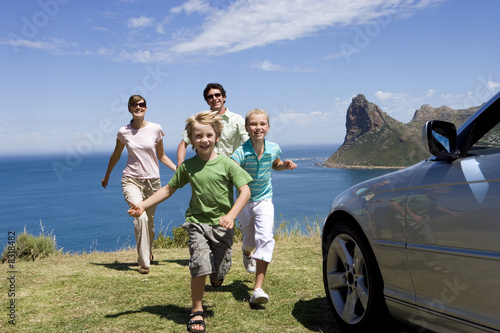 Foto: Family running towards parked car on clifftop overlooking Atlantic Ocean, smiling, portrait Family running towards parked car on clifftop overlooking Atlantic Ocean, smiling, portrait