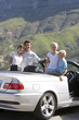 Photo: Family standing beside parked convertible car on mountain roadside, smiling, portrait Family standing beside parked convertible car on mountain roadside, smiling, portrait