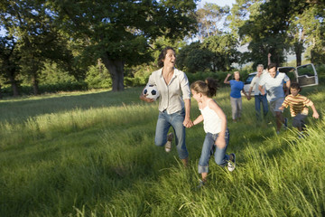 Photo: Multi-generational family playing with soccer ball in woodland clearing, mother and daughter (8-10) running away Multi-generational family playing with soccer ball in woodland clearing, mother and daughter (8-10) running away