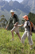 Photo: Senior couple, with rucksacks and sun hats, hiking on mountainside, holding hands, smiling, side view Senior couple, with rucksacks and sun hats, hiking on mountainside, holding hands, smiling, side view