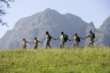 Photo: Multi-generational family hiking on mountain trail, walking in line, all holding hands, side view Multi-generational family hiking on mountain trail, walking in line, all holding hands, side view