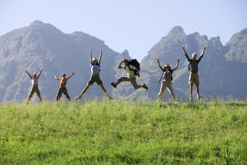 Photo: Multi-generational family hiking on mountain trail, jumping in line, arms up, front view, portrait Multi-generational family hiking on mountain trail, jumping in line, arms up, front view, portrait