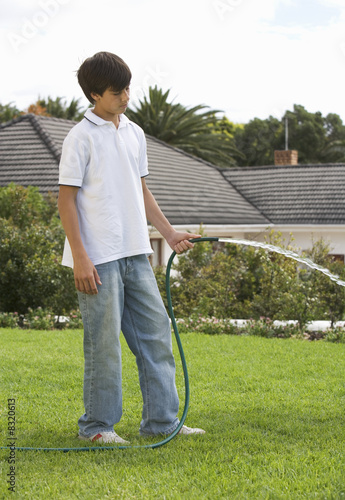 Photo: A young boy watering the garden with a hose A young boy watering the garden with a hose