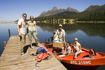 Photo: Multi-generational family loading motorboat with provisions on lake jetty, smiling, portrait Multi-generational family loading motorboat with provisions on lake jetty, smiling, portrait