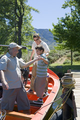 Photo: Boy (8-10) boarding motorboat moored at lake jetty, father and grandfather assisting, side view Boy (8-10) boarding motorboat moored at lake jetty, father and grandfather assisting, side view