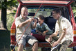 Photo: Boy (8-10) sitting in boot of parked SUV with father and grandfather, senior man holding fishing rod, smiling Boy (8-10) sitting in boot of parked SUV with father and grandfather, senior man holding fishing rod, smiling