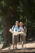 Photo: Senior couple hiking on woodland trail, man holding map, woman using hiking pole, smiling, front view Senior couple hiking on woodland trail, man holding map, woman using hiking pole, smiling, front view