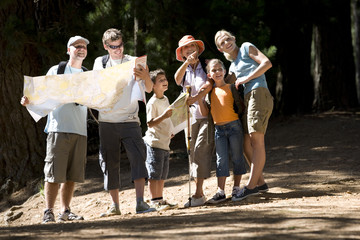 Photo: Multi-generational family hiking along woodland trail, men looking at map, senior woman pointing Multi-generational family hiking along woodland trail, men looking at map, senior woman pointing