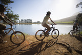 Photo: Family mountain biking along lakeside woodland trail, side view (lens flare, backlit) Family mountain biking along lakeside woodland trail, side view (lens flare, backlit)