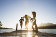 Photo: Family, in swimwear, running along jetty, jumping into lake at sunset, rear view (surface level, lens flare) Family, in swimwear, running along jetty, jumping into lake at sunset, rear view (surface level, lens flare)