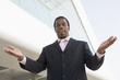 Businessman standing outdoors by building with hands out smiling