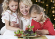 A grandmother and her granddaughters looking at a Christmas pudding