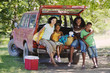 Photo: Family sitting in back of parked SUV, unloading provisions on camping trip, smiling, portrait Family sitting in back of parked SUV, unloading provisions on camping trip, smiling, portrait