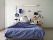 Male patient lying in hospital bed, using laptop, face obscured, front view
